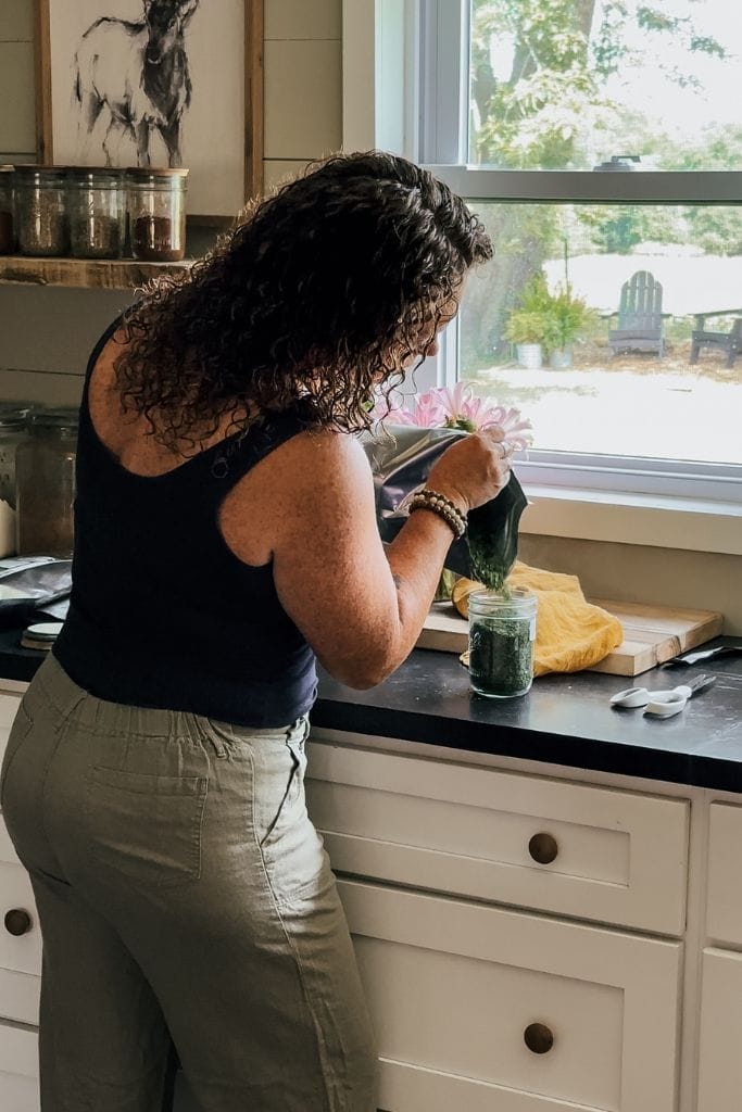 a lady pouring dried herbs into a glass mason jar