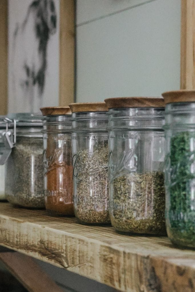 a row of jars filled with spices and herbs that are pantry staples