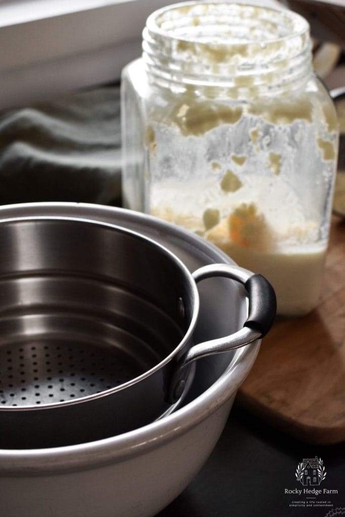 a colander sitting inside of a white bowl ready to have buttermilk and butter dumped into it. 