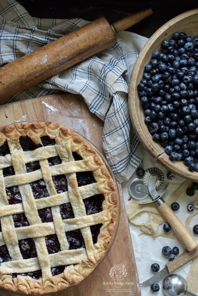 Blueberry pie next to a bowl of fresh picked blueberries
