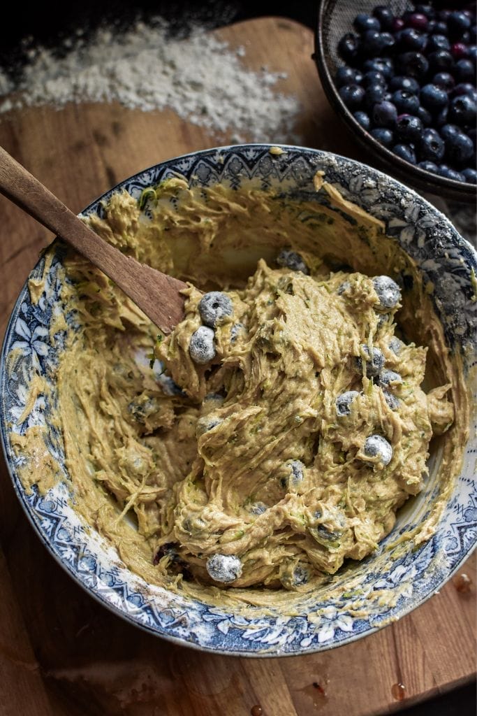 A blue and white bowl filled with batter to make zucchini bread with blueberries