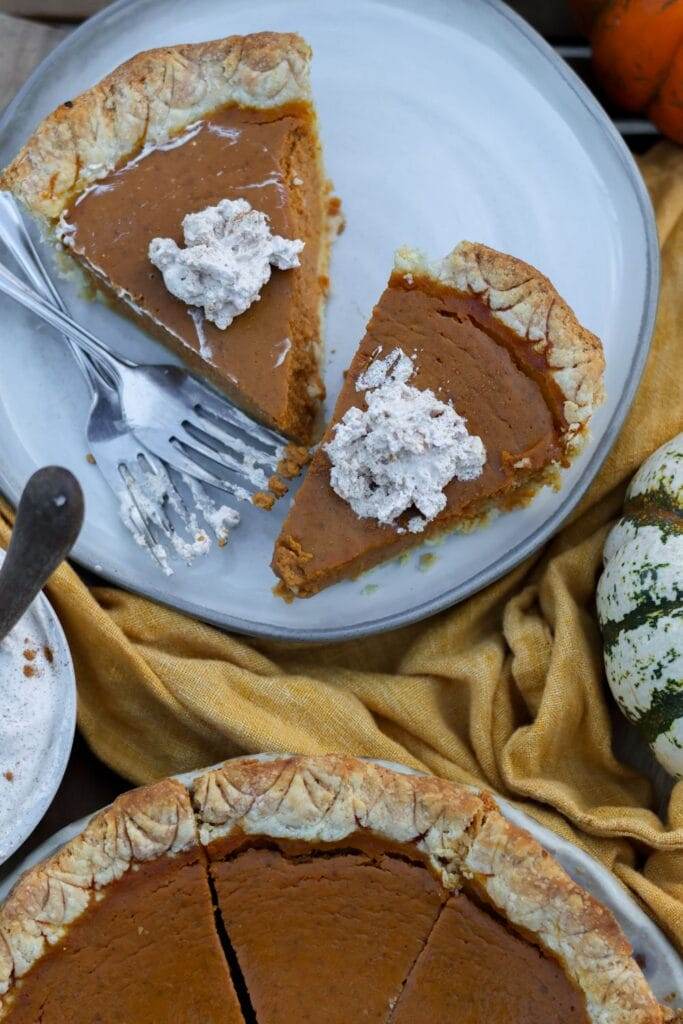 two slices of pumpkin pie on a plate that are topped with homemade whipped cream