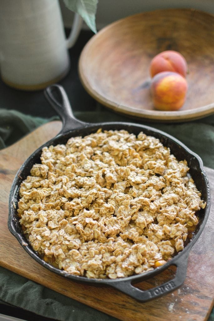 peach crisp in a cast iron skillet with the oat topping