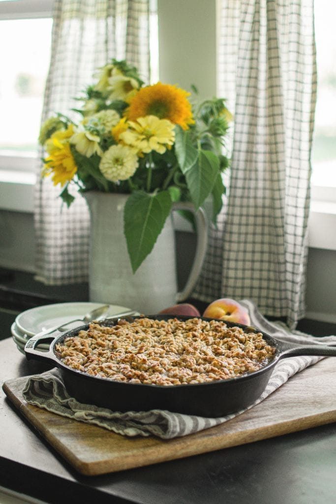 peach crisp in a cast iron skillet, with a golden brown oat crumble topping and juicy peach filling bubbling around the edges
