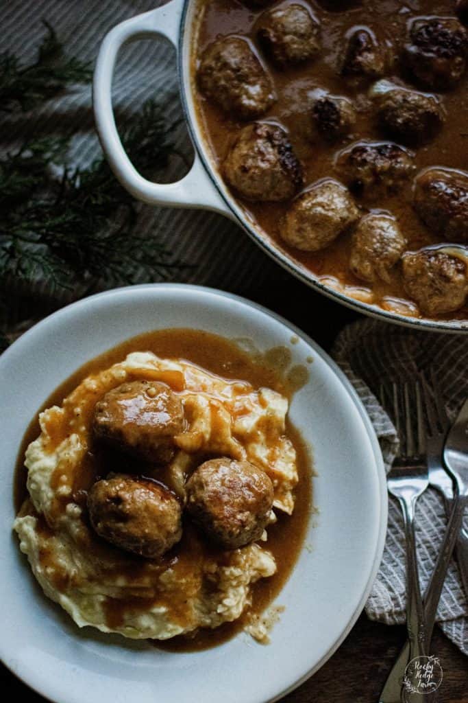 A plate full of mashed potatoes topped with meatballs and gravy