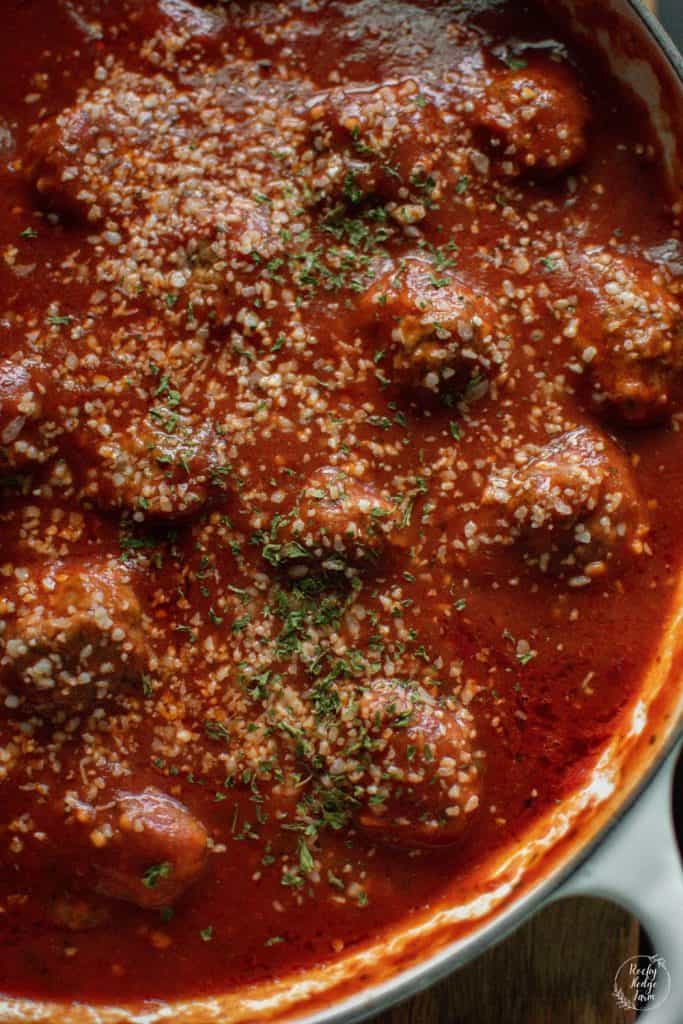 An enameled cast iron skillet filled with simmering Italian meatballs in tomato sauce. 