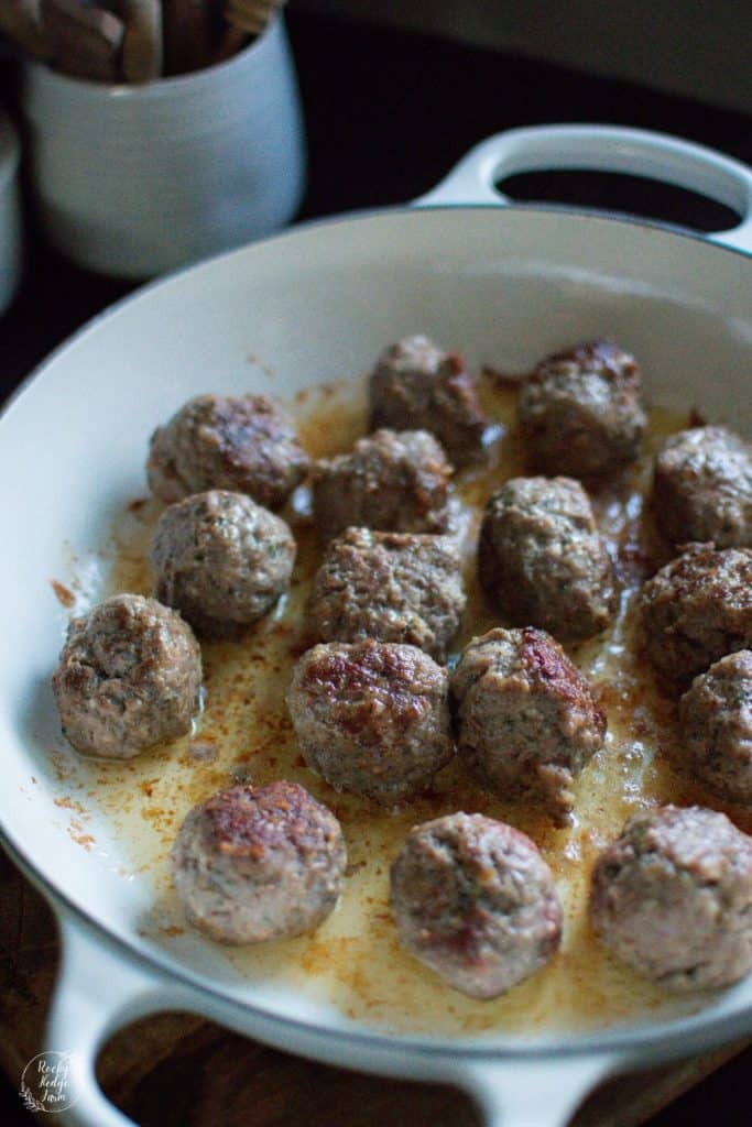 A cast iron skillet filled with Italian sausage meatballs cooking on the stovetop