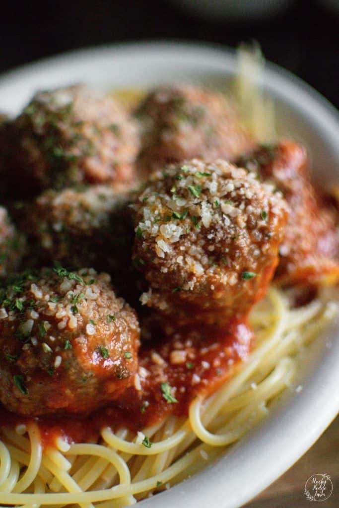 A plate full of traditional Italian meatballs over the top of spaghetti noodles. 