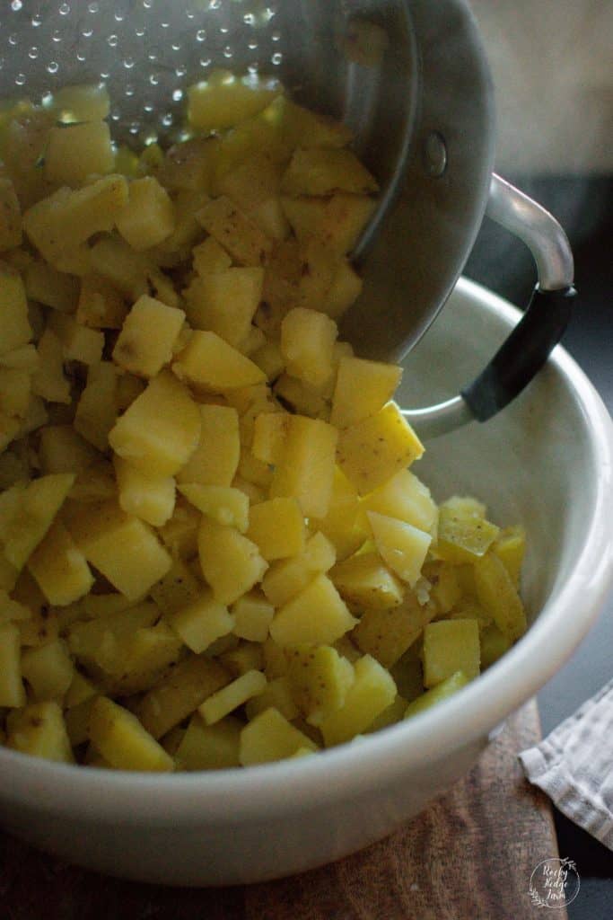 adding hot potatoes to a large mixing bowl to make potato salad