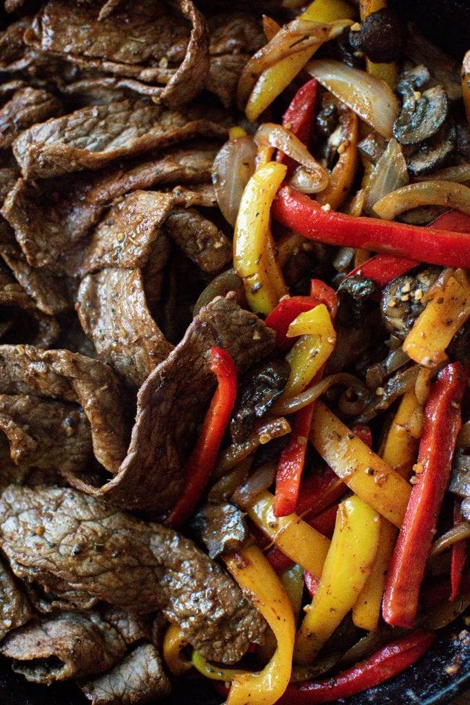 A skillet filled with steak strips and red and yellow bell peppers making fajitas