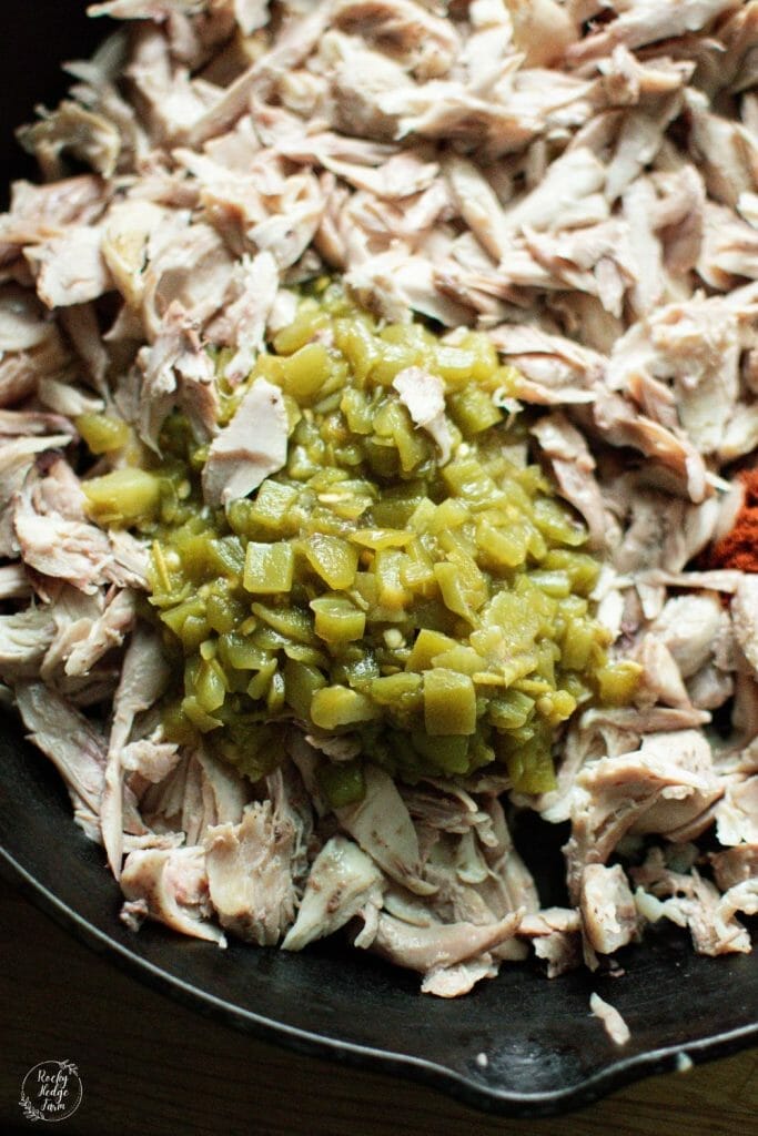 Savory shredded chicken tacos cooking in a cast iron skillet with green chiles
