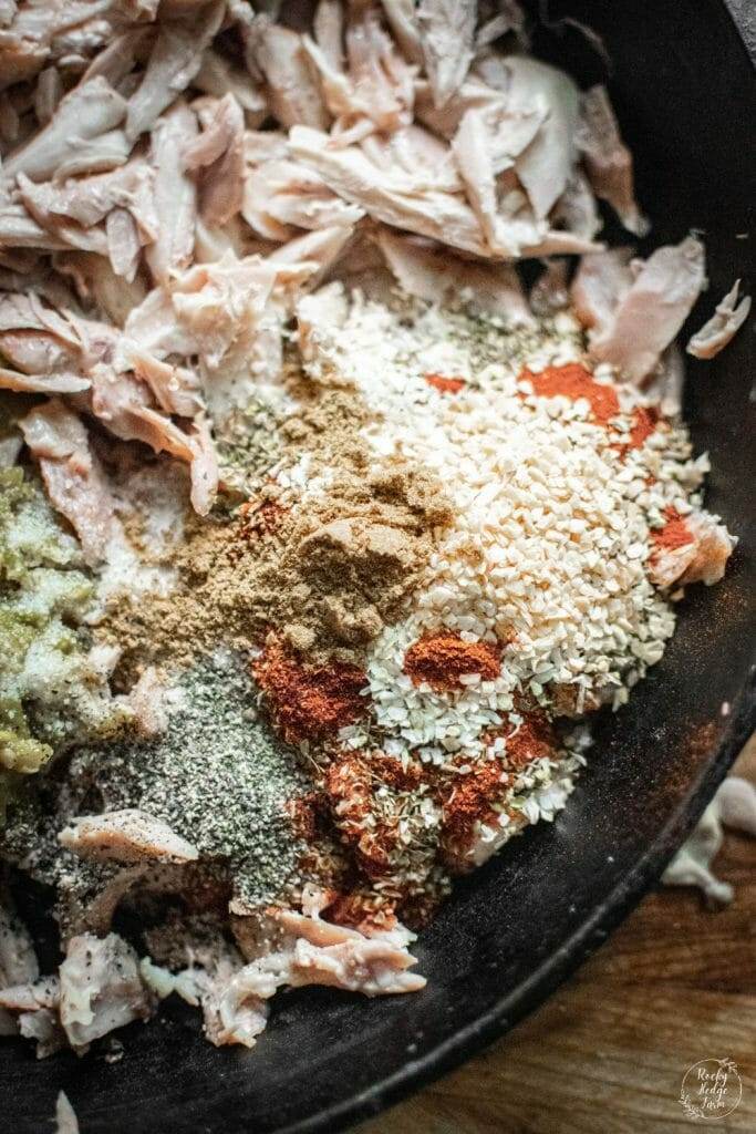 Savory shredded chicken tacos cooking in a cast iron skillet with spices and green chiles