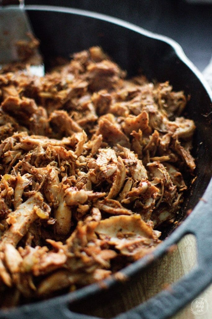 Juicy and flavorful shredded chicken taco meat sizzling in a cast iron skillet with spices. 