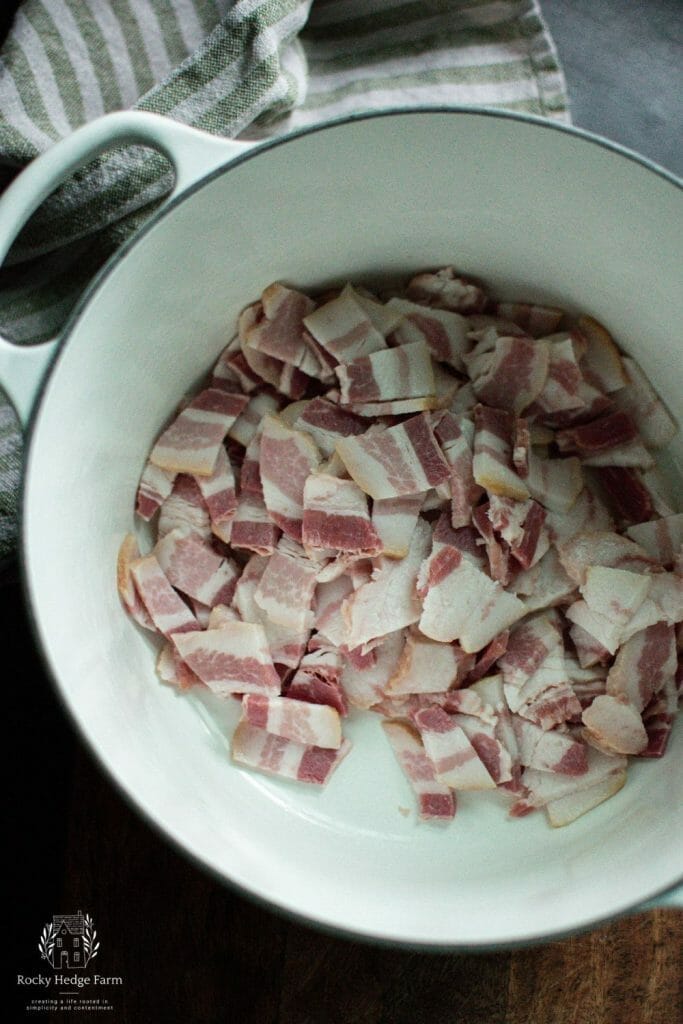 Cooking bacon in a white cast iron dutch oven for cowboy beans
