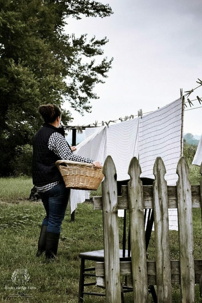 Sarah at Rocky Hedge Farm standing at the clothes line with a laundry basket on her hip taking laundry off the line