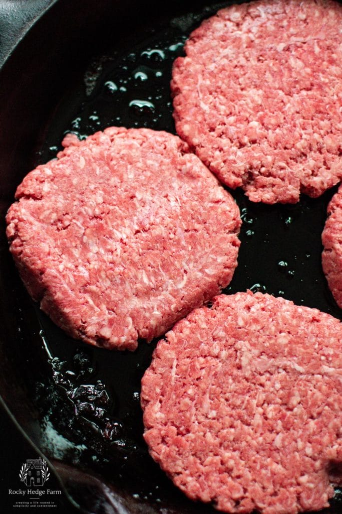 raw burgers cooking in a cast iron skillet
