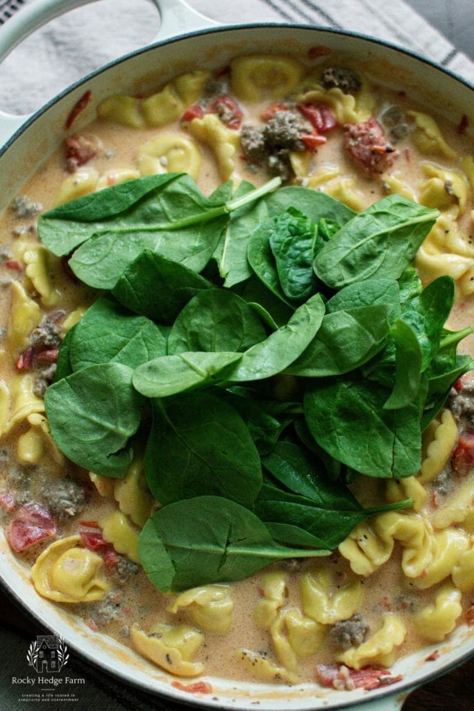 Adding spinach to the sausage tortellini skillet