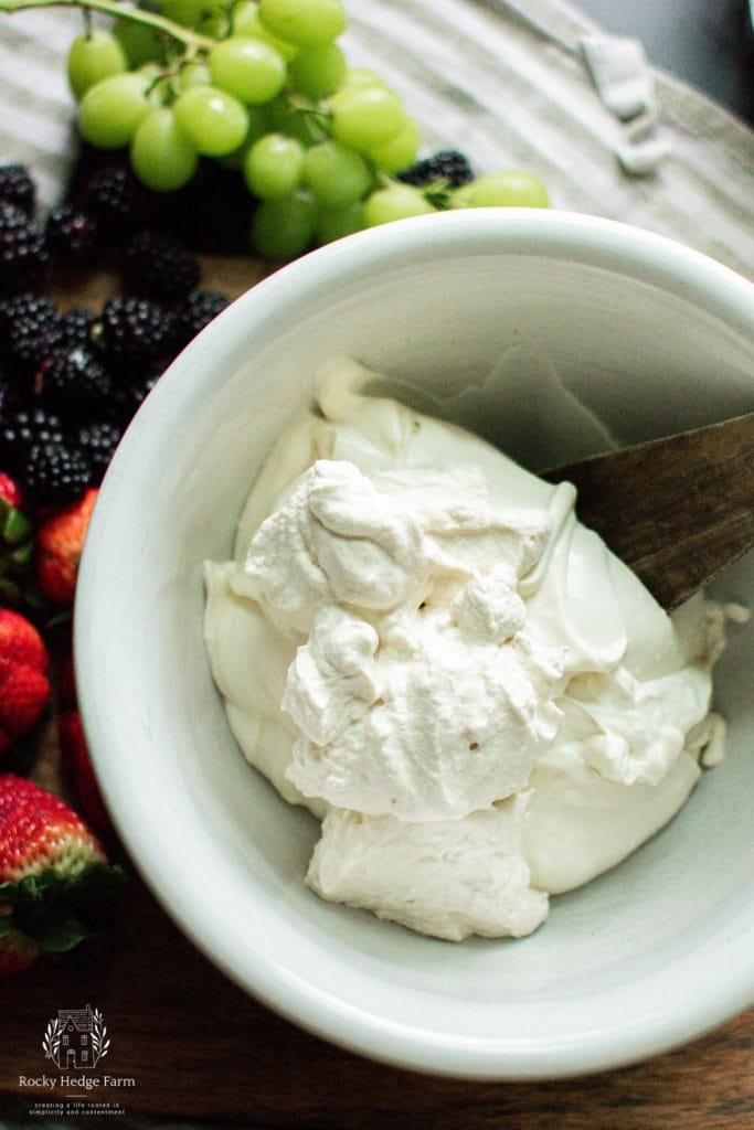 A white bowl with cream cheese, yogurt and honey ready to be mixed with homemade whipped cream to make homemade cream cheese fruit dip.