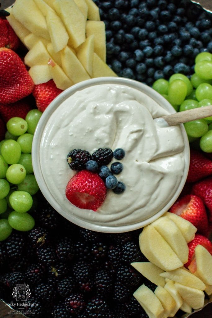A colorful assortment of fresh fruits arranged on a platter, accompanied by a bowl of creamy, white cream cheese dip