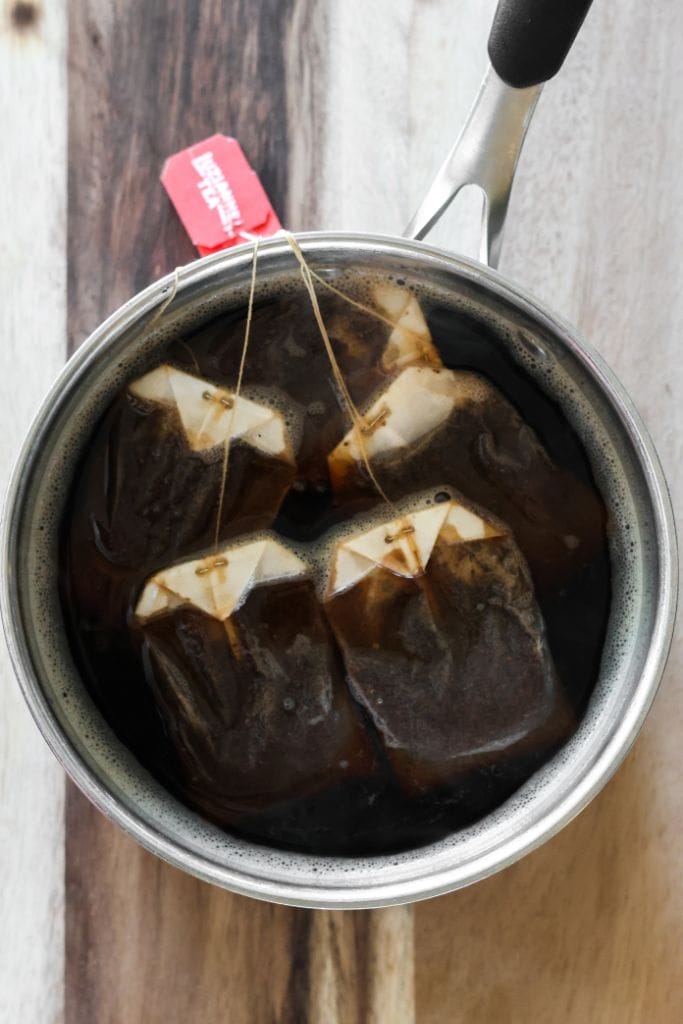 Four tea bags in a pot of clear boiling water.