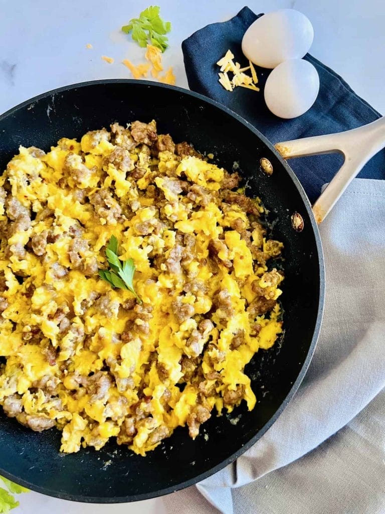 A breakfast scramble with eggs, sausage, and cheese cooking in a skillet.