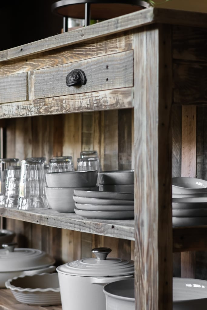 Kitchen island crafted from reclaimed wood, boasting a built-in seating area for two and maximizing functionality with its shelves and cabinets.