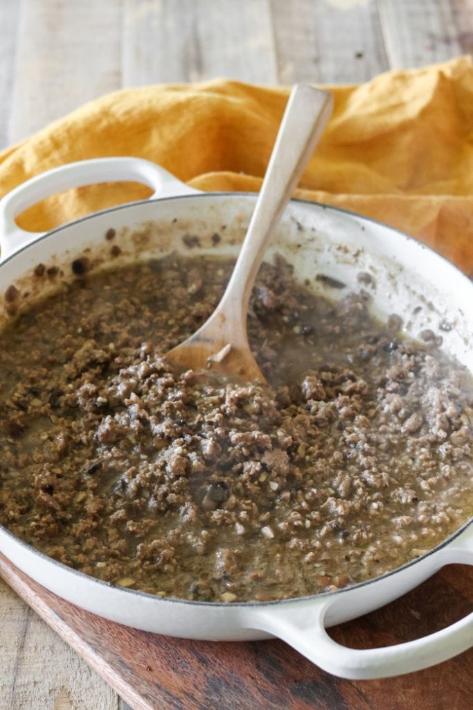 a skillet filled with ground beef, mushrooms and beef broth