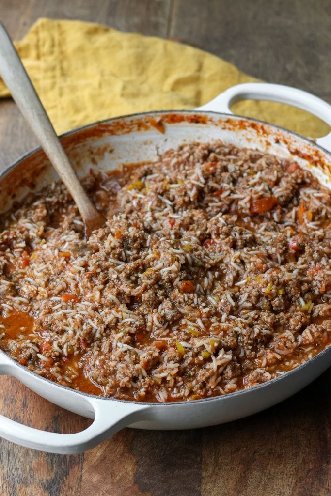 Large white skillet filled with a savory ground beef and pepper skillet mixture. The dish includes cooked ground beef, diced peppers, rice, and tomato sauce.