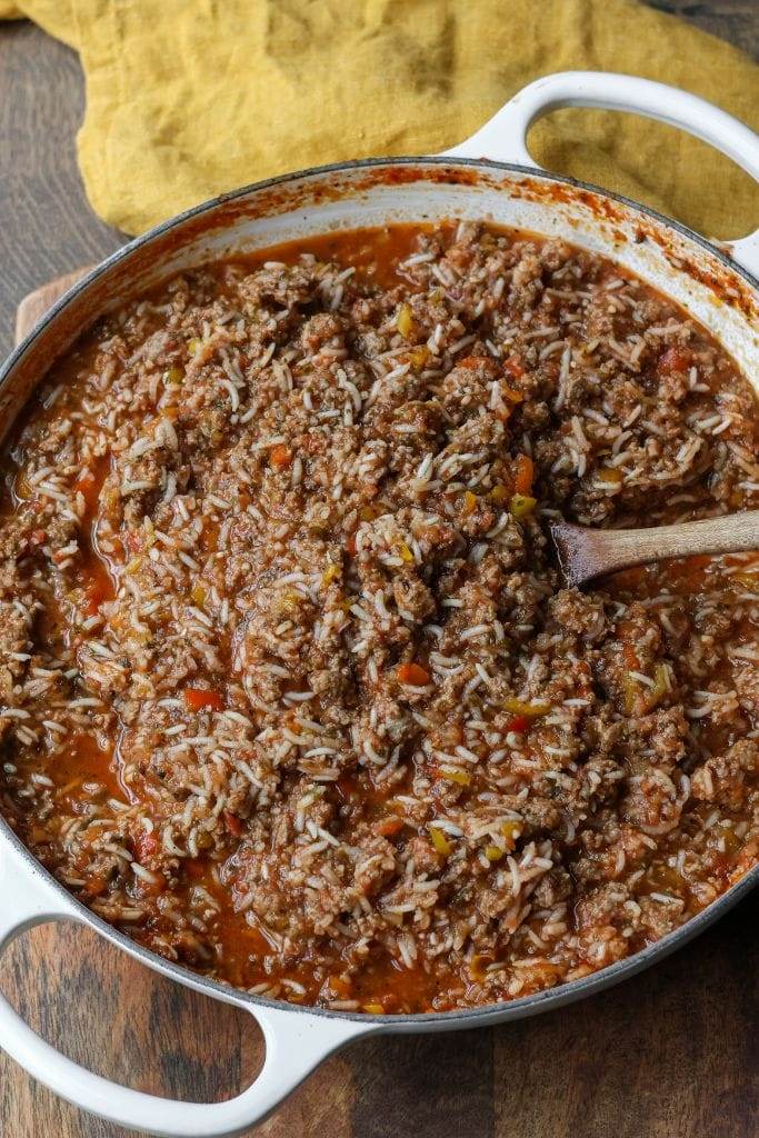 Skillet with ground beef, vegetables, rice, and tomato sauce ready to simmer.