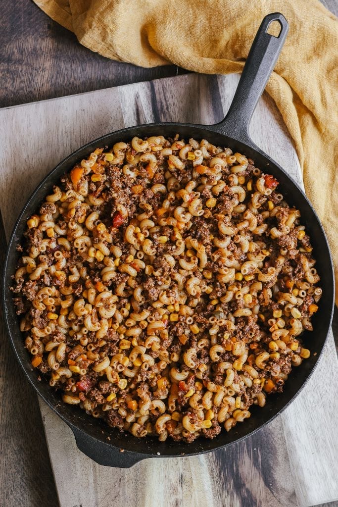 A skillet filled with ground beef, noodles, corn, and diced tomatoes