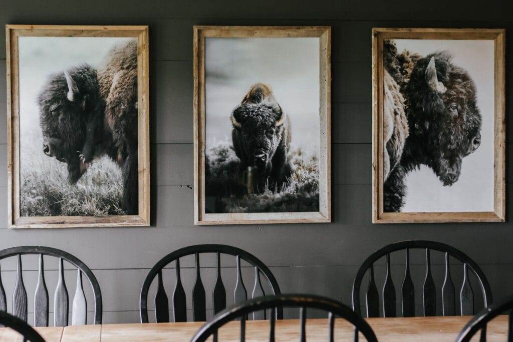 Full view of a cozy dining room with a cabincore aesthetic, featuring moody walls, bison prints, and rustic decor.