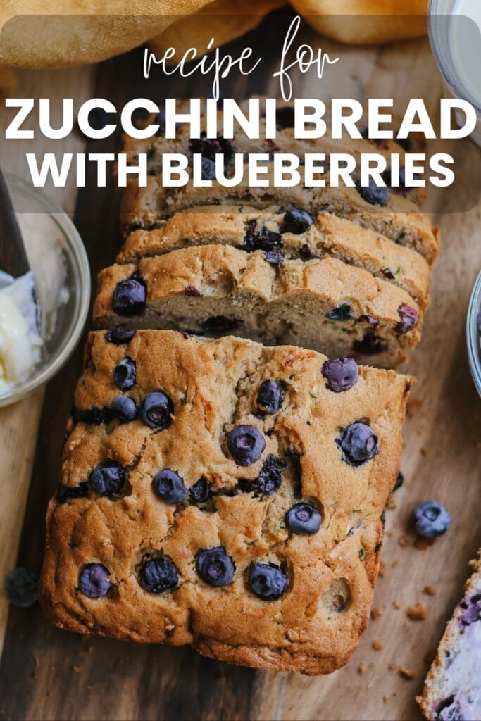 loaf of zucchini blueberry bread partially sliced on with fresh blueberries nearby.