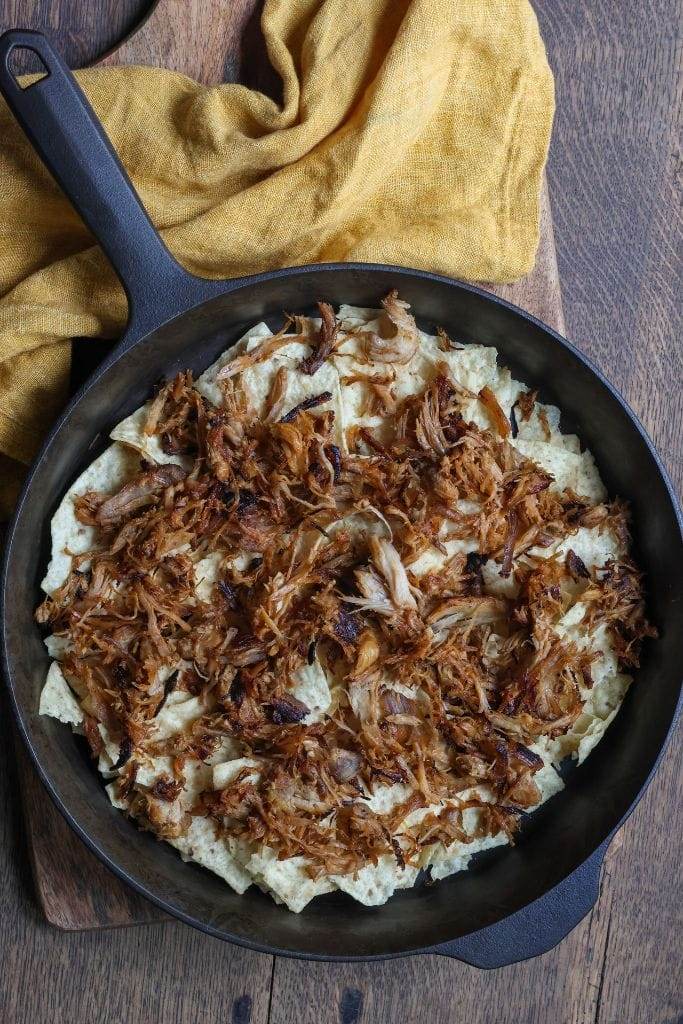 a cast iron skillet filled with tortilla chips and a layer of bbq pork for nachos