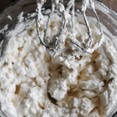 hand mixer and glass bowl with homemade whipped cream that is made with maple syrup and vanilla