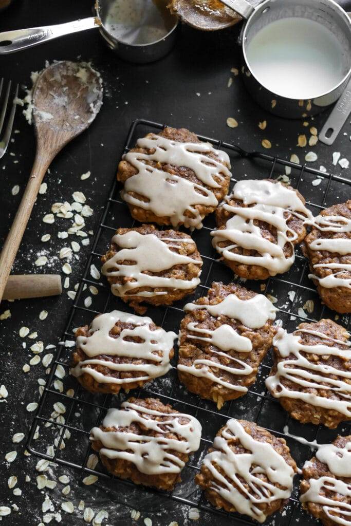 An overhead view of pumpkin oatmeal cookies drizzled with cinnamon maple glaze, with a few cookies stacked on a cooling rack