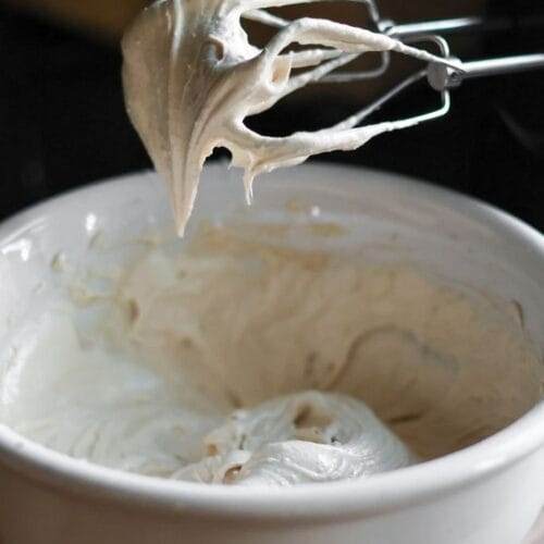 Close-up of cinnamon maple cream cheese frosting clinging to the blades of a hand mixer