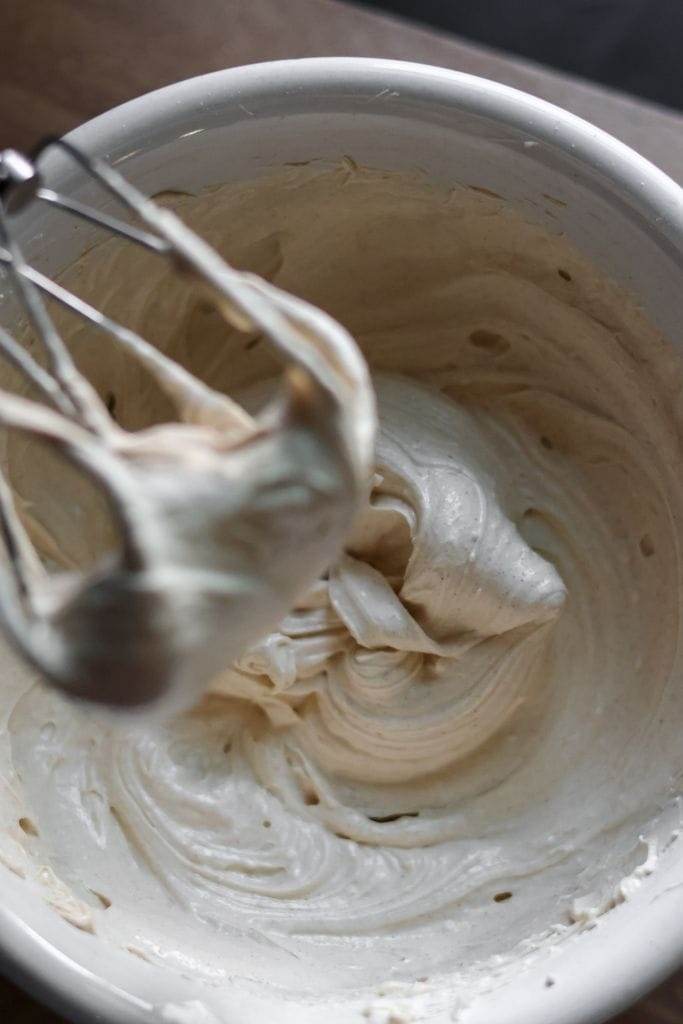 A mixing bowl filled with light and fluffy cinnamon maple cream cheese frosting, ready to be spread on baked goods.