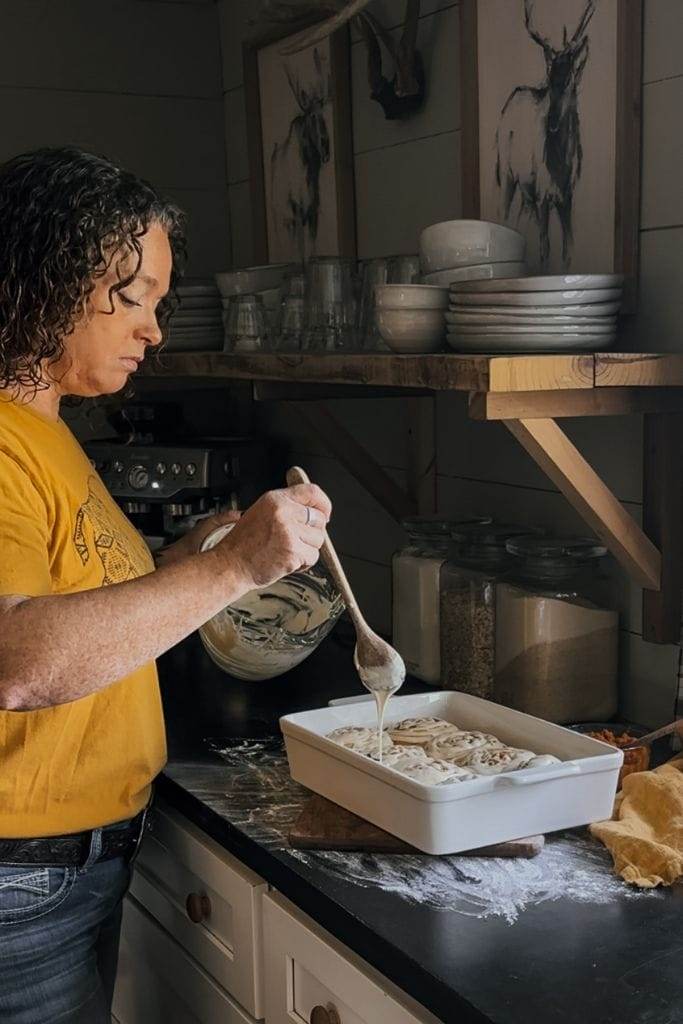 A person drizzling cinnamon maple cream cheese frosting over a dessert, adding a sweet finishing touch to the dish.