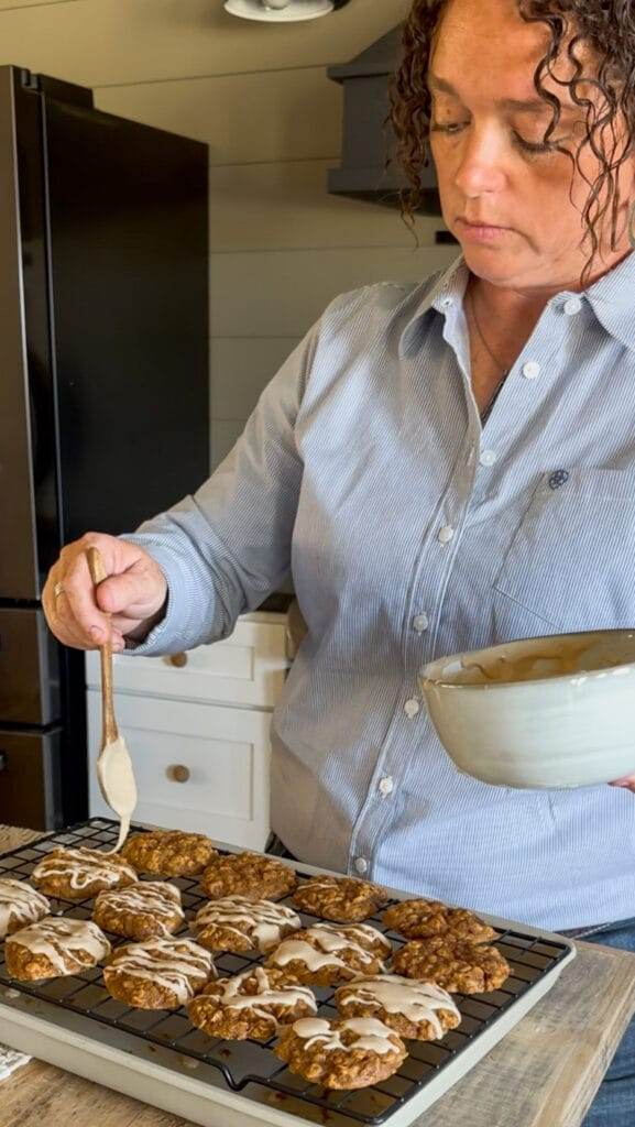 A human drizzling cinnamon maple glaze over a freshly baked pumpkin oatmeal cookie