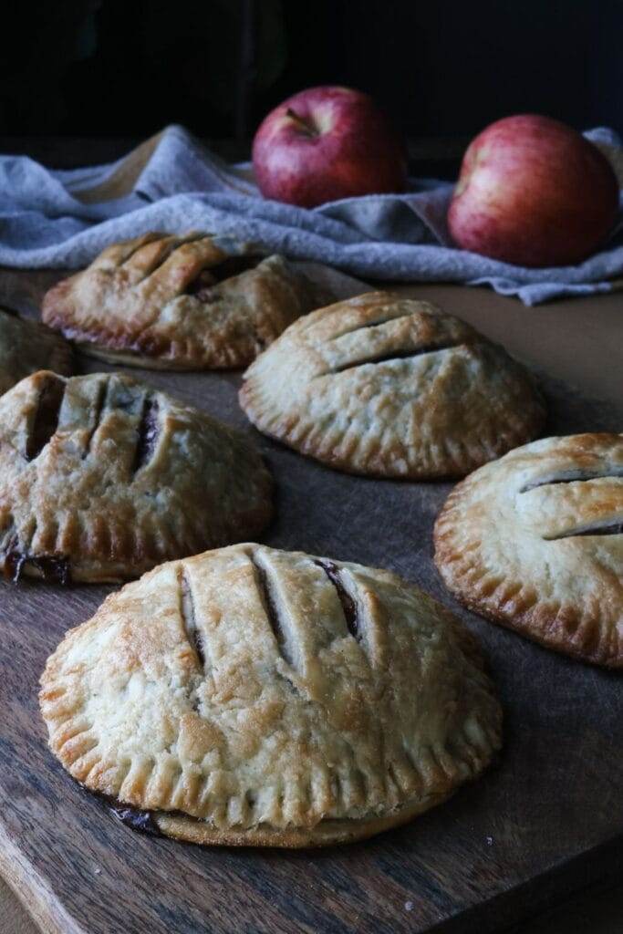 A batch of freshly baked apple hand pies cooling on a rack, with golden crusts and bubbling apple filling peeking out