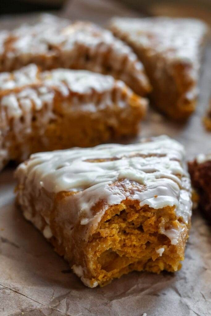 Close-up of a freshly baked maple pumpkin scone with a bite taken out, showing the soft, flaky texture and warm pumpkin filling inside.