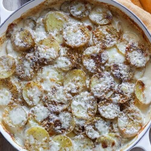 Cheesy scalloped potatoes with fresh thyme, served warm in a cast iron skillet, showing a crispy, golden-brown top.