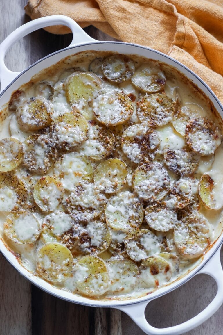 Cheesy scalloped potatoes with fresh thyme, served warm in a cast iron skillet, showing a crispy, golden-brown top.