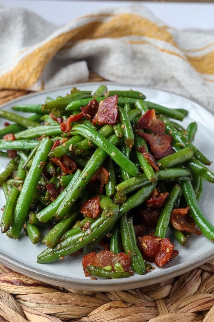 Freshly cooked green beans topped with bacon, served on a white plate.