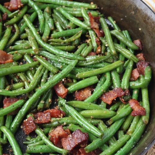 Cooked green beans with bacon, onion, and garlic in a cast iron skillet.