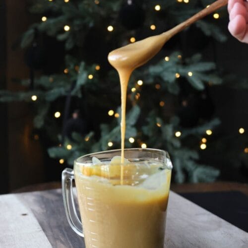 Homemade sweetened condensed milk, creamy and thick, in a mason jar with a golden hue, placed on a wooden kitchen counter.