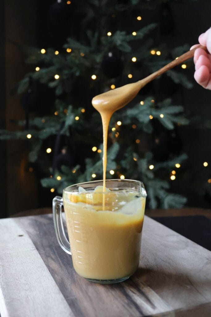 Homemade sweetened condensed milk, creamy and thick, in a mason jar with a golden hue, placed on a wooden kitchen counter.