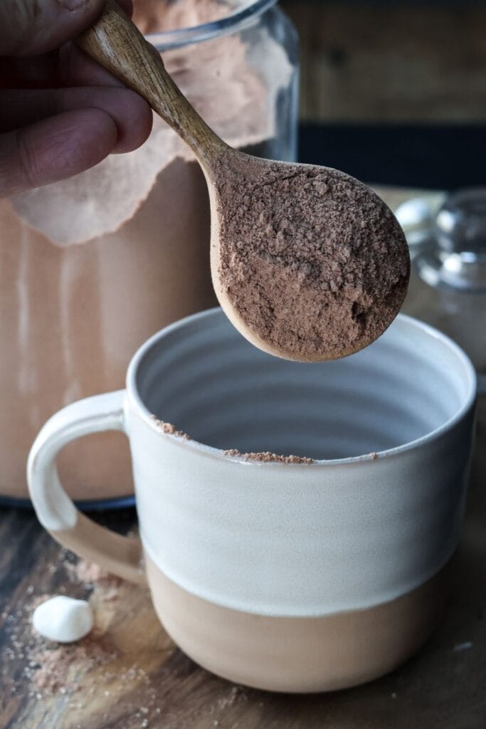 a spoonful of hot cocoa mix being put into a coffee mug